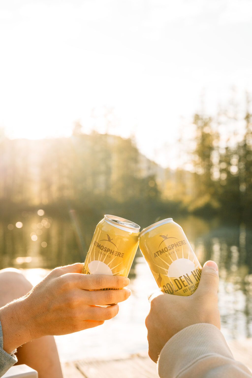 Two cans of Golden Hour clinking together at sunset