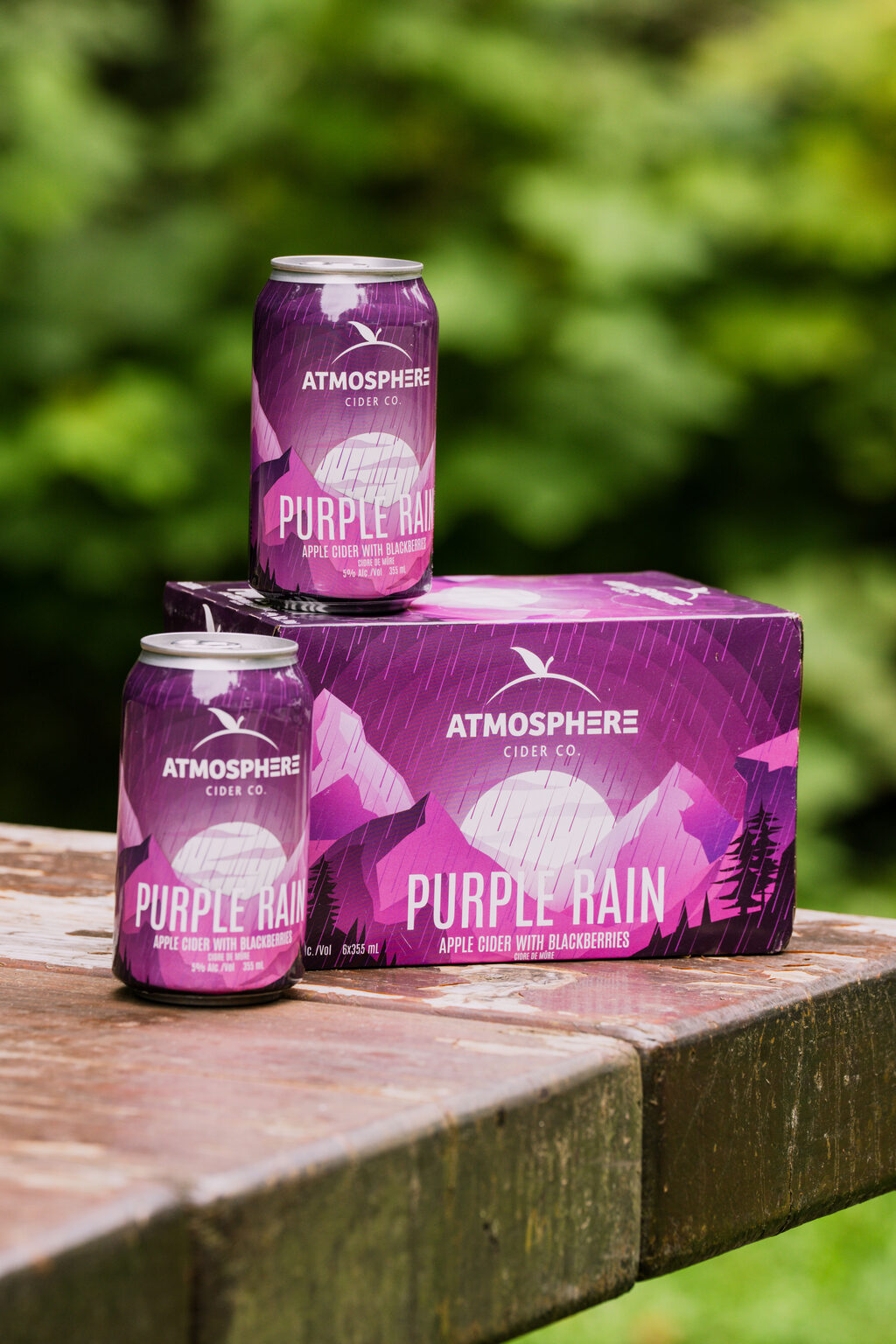 Purple Rain cans and 6-pack on a picnic table in the forest