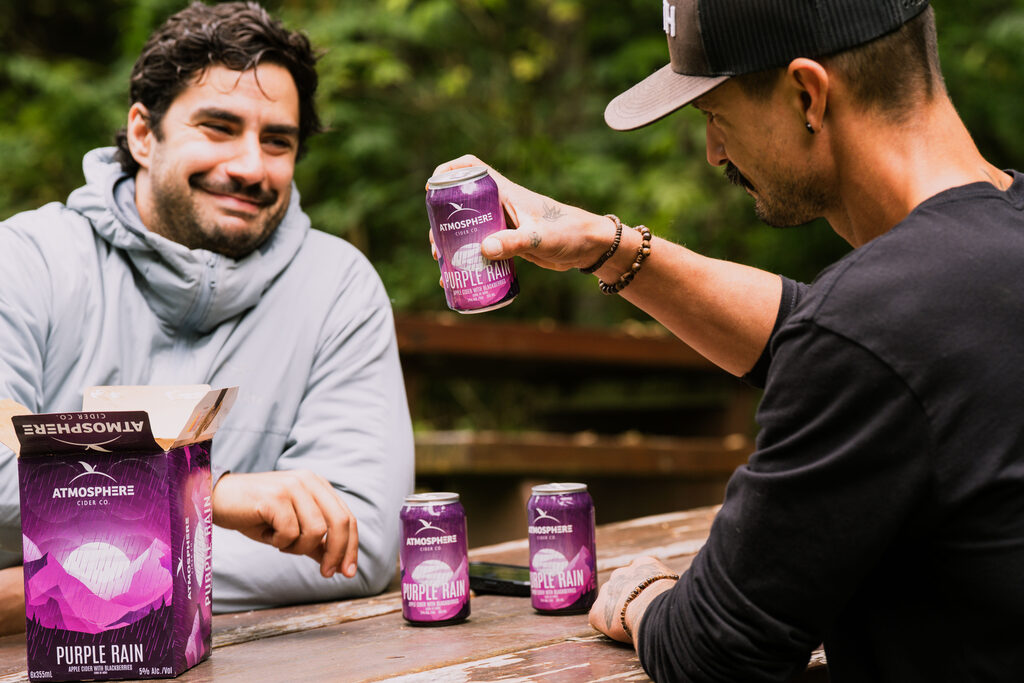 Friends cheersing cans of Purple Rain at a picnic table